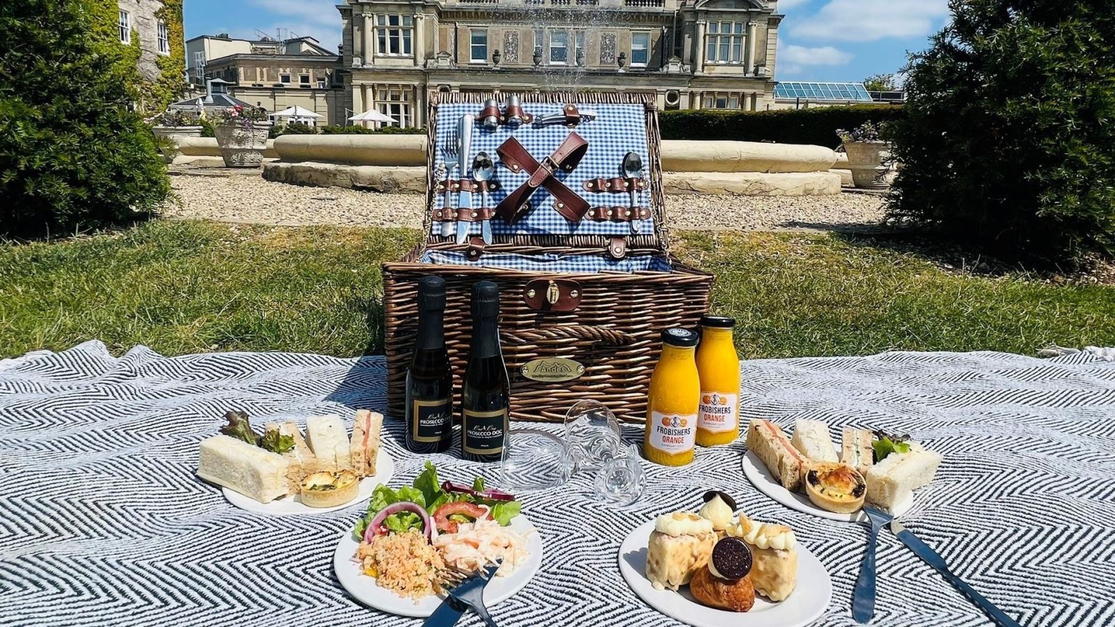 Picnic basket on a blanket with drinks and plates of food in front of Down Hall Estate, Essex